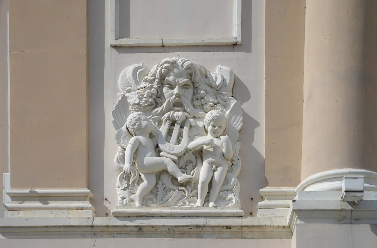 Sculpted Beaux-Arts relief on the Saigon Opera House façade with a bearded classical figure and two winged cherubs holding a lyre
