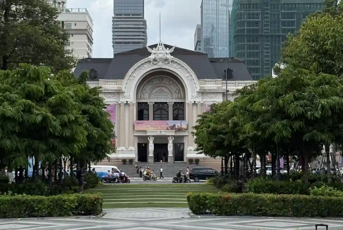Saigon Opera House framed by tropical trees on Lam Son Square with modern District 1 skyscrapers rising behind its slate roof, Ho Chi Minh City