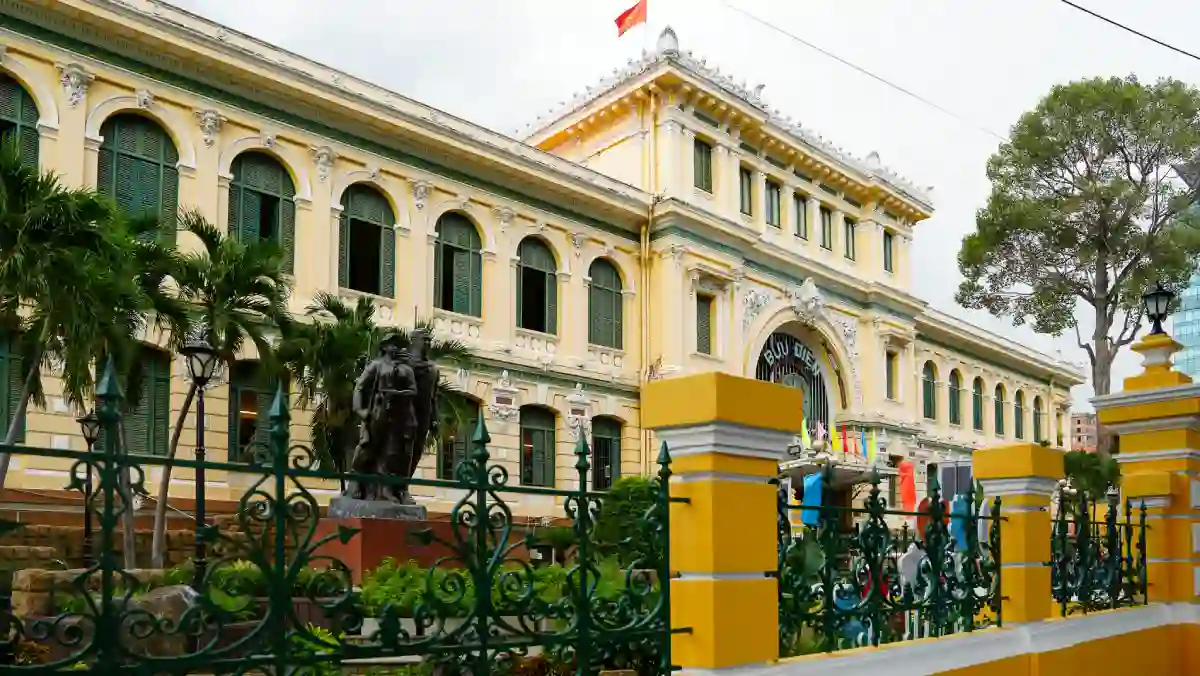 Saigon Central Post Office — yellow Beaux-Arts façade with arched windows, bronze statue and green wrought-iron fence in District 1, Ho Chi Minh City