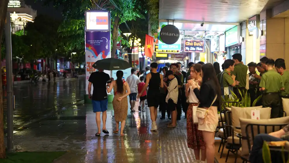 Locals strolling along Nguyen Hue Walking Street in District 1, Ho Chi Minh City after an evening rain, with wet pavement reflecting shopfront lights