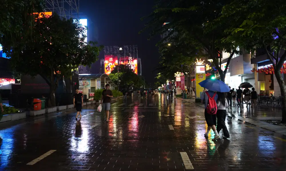 Nguyen Hue Walking Street at night in the rain — wet pavement reflecting LED screens and pedestrians with umbrellas in District 1, Saigon
