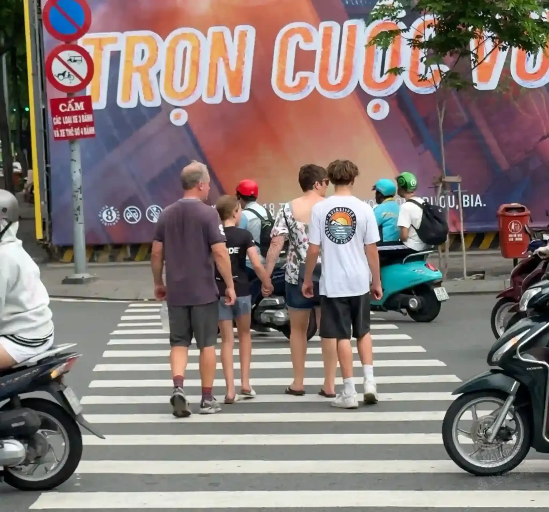 A foreign tourist family stands frozen at a District 1 crosswalk in Ho Chi Minh City as motorbikes stream past in front of them