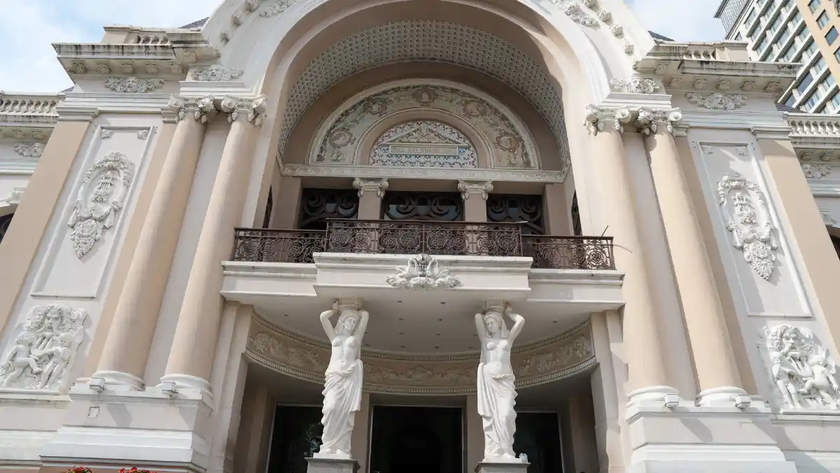 Close-up of the two sculpted female caryatids supporting the wrought-iron balcony above the main entrance of the Saigon Opera House in District 1, Ho Chi Minh City