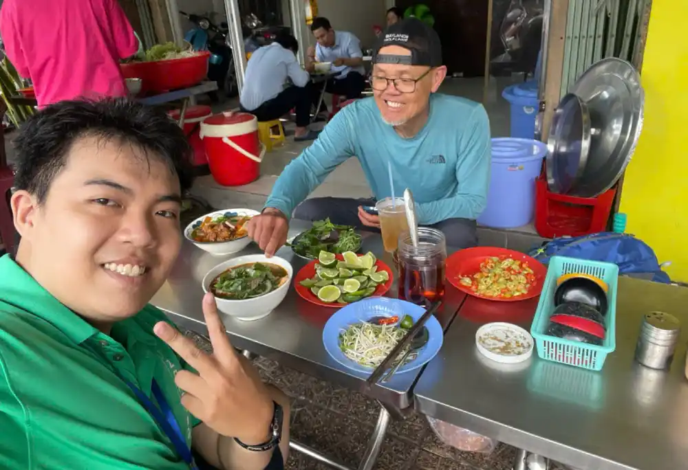 Local Saigon guide and a guest sharing bowls of bun bo Hue, fresh herbs, lime, bean sprouts and iced tea at a street food spot in District 1, Ho Chi Minh City