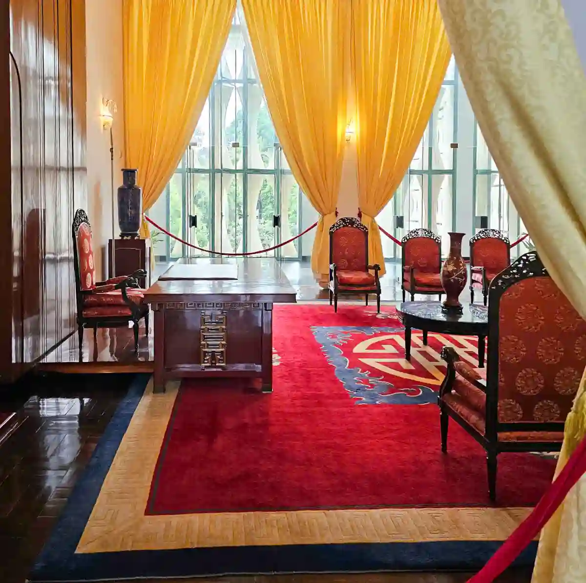Presidential reception room inside Independence Palace with red carpet, golden yellow drapes and traditional Vietnamese hardwood chairs