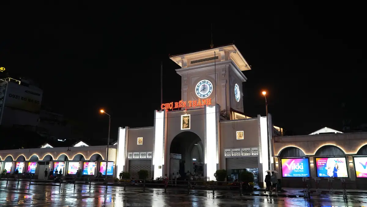 Ben Thanh Market clock tower with the illuminated 'Chợ Bến Thành' sign glowing above the south gate at night in District 1, Ho Chi Minh City
