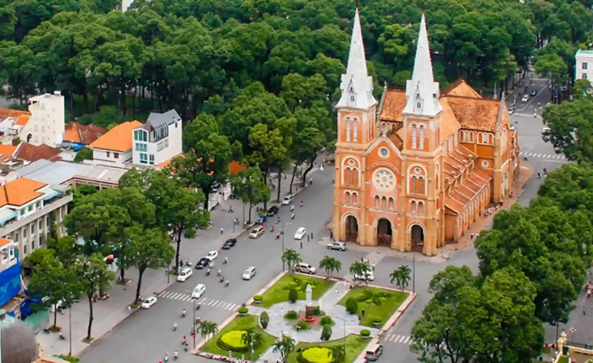 Aerial view of Notre Dame Cathedral Saigon with its twin bell towers, terracotta-tiled roof, and the leafy park square of District 1, Ho Chi Minh City