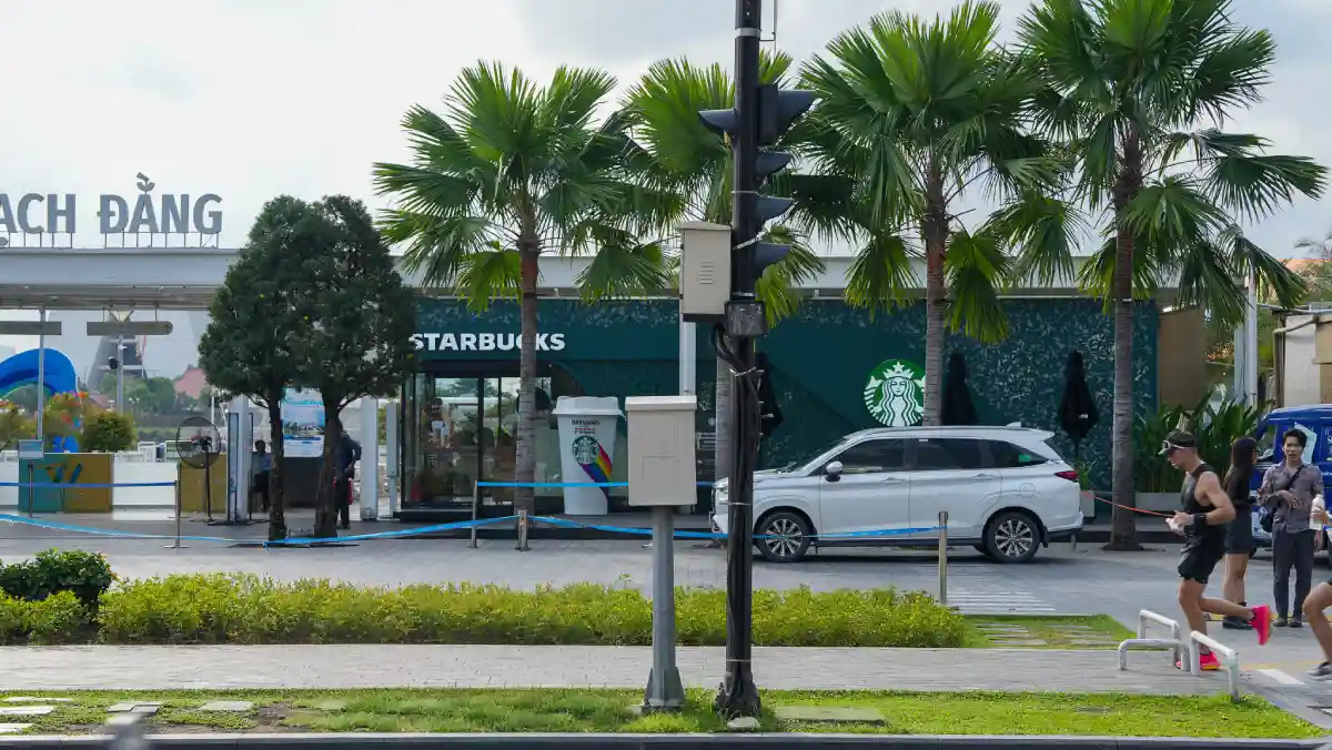 Palm-lined promenade at Bach Dang Wharf with joggers passing the Starbucks pavilion and Bach Dang sign in District 1, Ho Chi Minh City