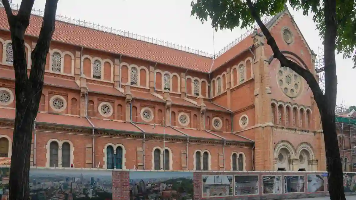 Notre Dame Cathedral Saigon — red brick side façade with rose windows and Romanesque arches, framed by tropical trees in District 1, Ho Chi Minh City
