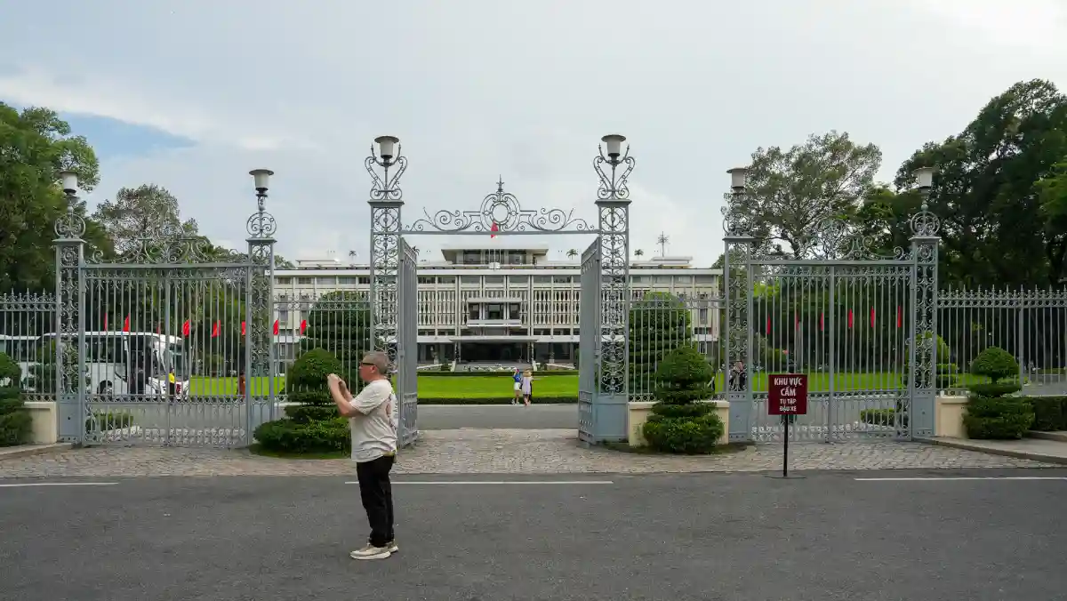 Visitor photographing the ornate wrought-iron main gates of Independence Palace in District 1, Ho Chi Minh City