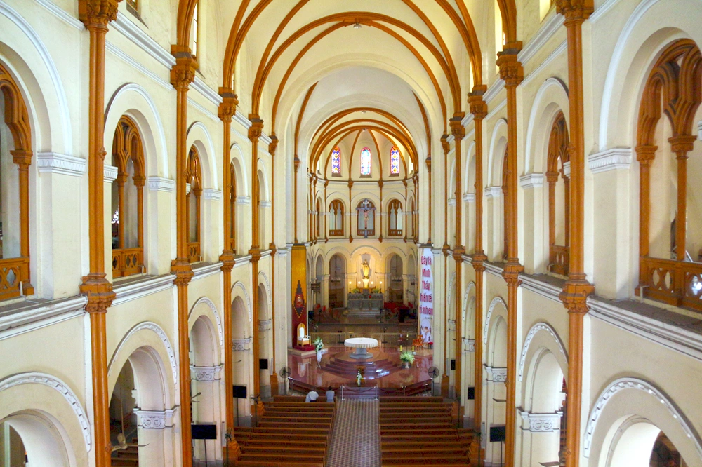 Interior of Notre Dame Cathedral Saigon viewed from the upper gallery, showing the central nave, soaring arched columns, wooden pews and stained-glass windows above the altar