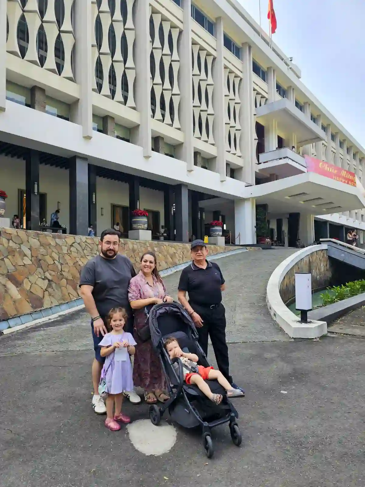 Multigenerational family with a stroller posing in front of the modernist entrance ramp of Independence Palace in Ho Chi Minh City