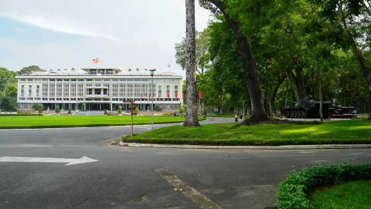 Independence Palace seen from across its tree-shaded grounds with a historic military tank on display in Ho Chi Minh City