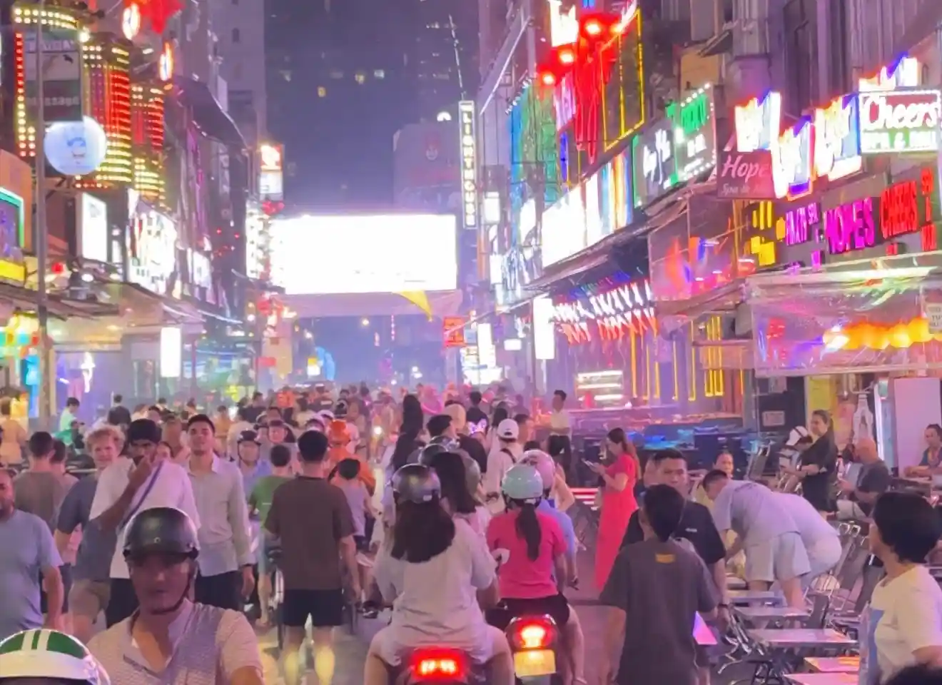 Crowds of locals and travellers walking through Bui Vien Walking Street in District 1, Saigon at night, surrounded by neon bar signs and colourful LED lights