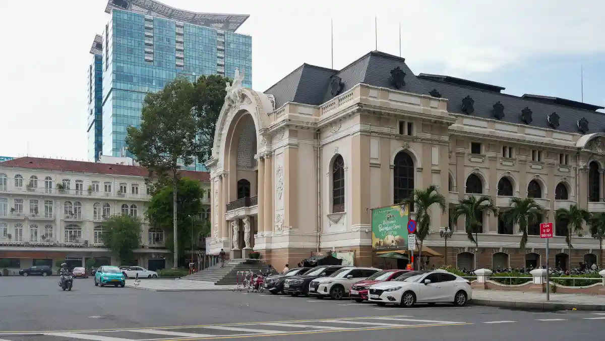Side profile of the Saigon Opera House with a glass-and-steel skyscraper rising behind its slate Mansard roof on Lam Son Square, District 1, Ho Chi Minh City