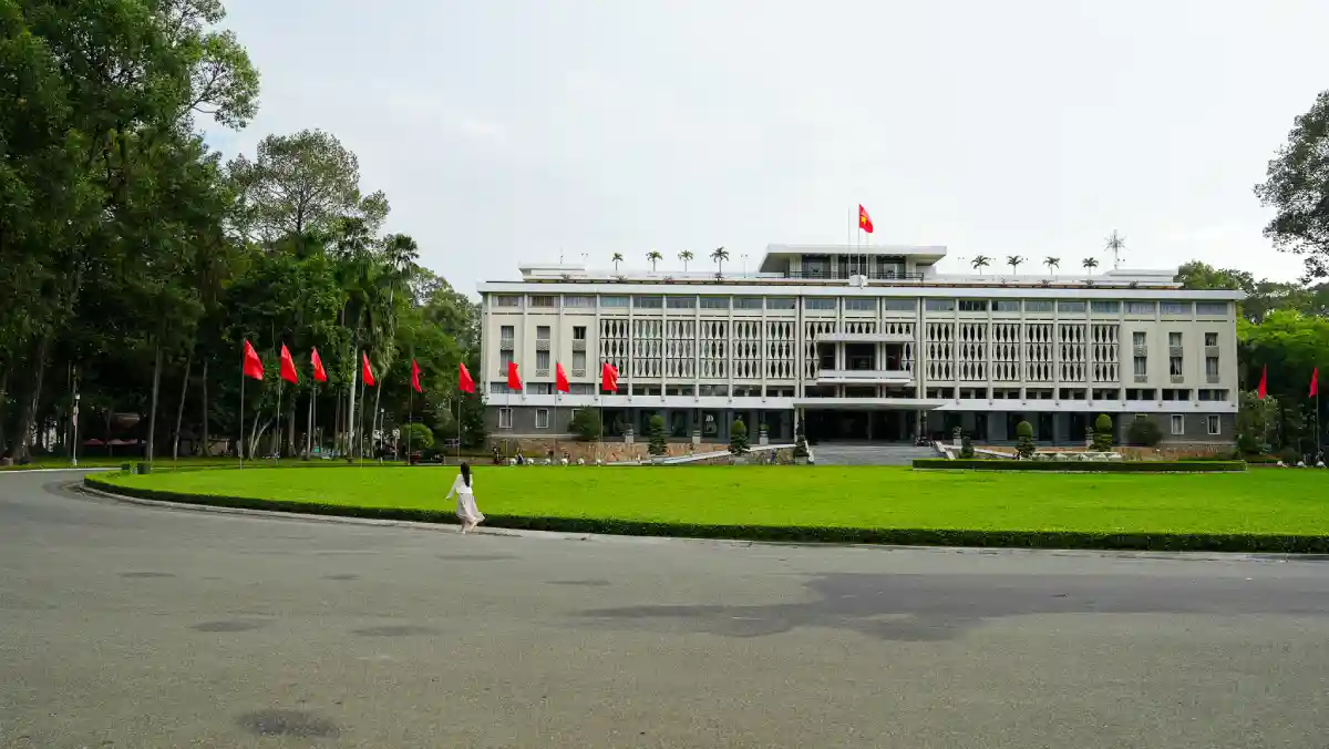 Modernist front façade of Independence Palace with rows of red Vietnamese flags lining the lawn in Ho Chi Minh City