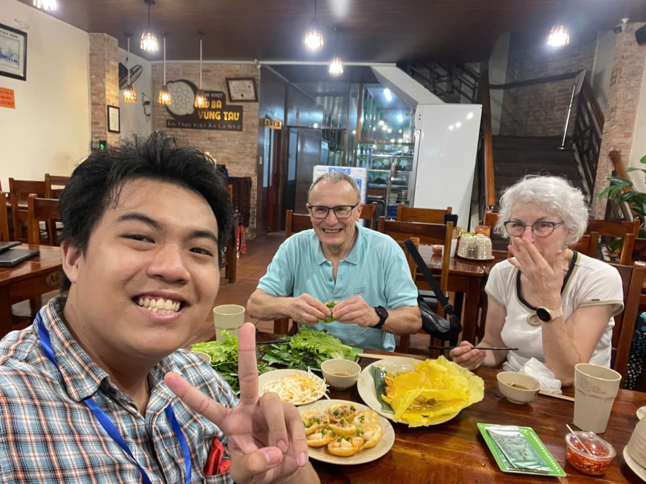 Local Saigon guide sharing a banh khot and Vietnamese herbs dinner with international guests at a family restaurant in Ho Chi Minh City