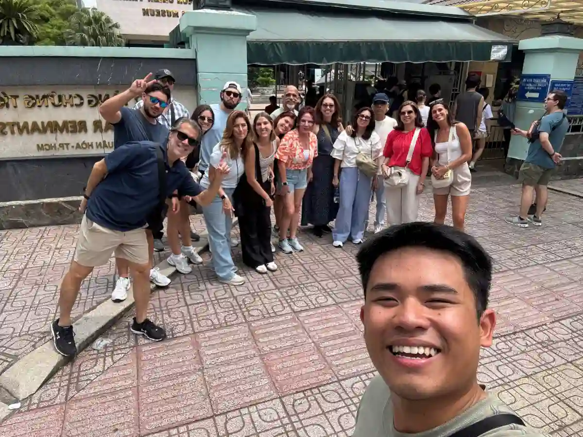 Free Walking Tours Saigon local guide takes a group selfie with international travellers in front of the War Remnants Museum entrance in District 3, Ho Chi Minh City