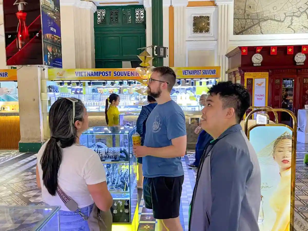 Local guide explaining the history of Saigon Central Post Office to travellers inside the colonial-era hall in District 1, Ho Chi Minh City