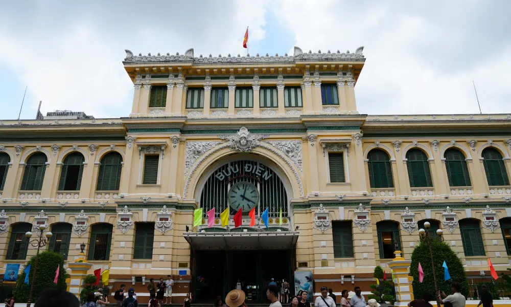 Saigon Central Post Office (Bưu Điện) — yellow French colonial façade with arched entrance, clock and colourful flags in District 1, Ho Chi Minh City