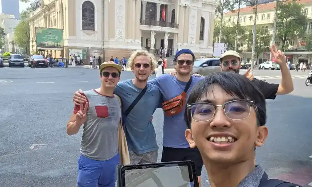 Local guide takes a selfie with a small group of international travellers in front of the Saigon Opera House during a free walking tour in District 1, Ho Chi Minh City