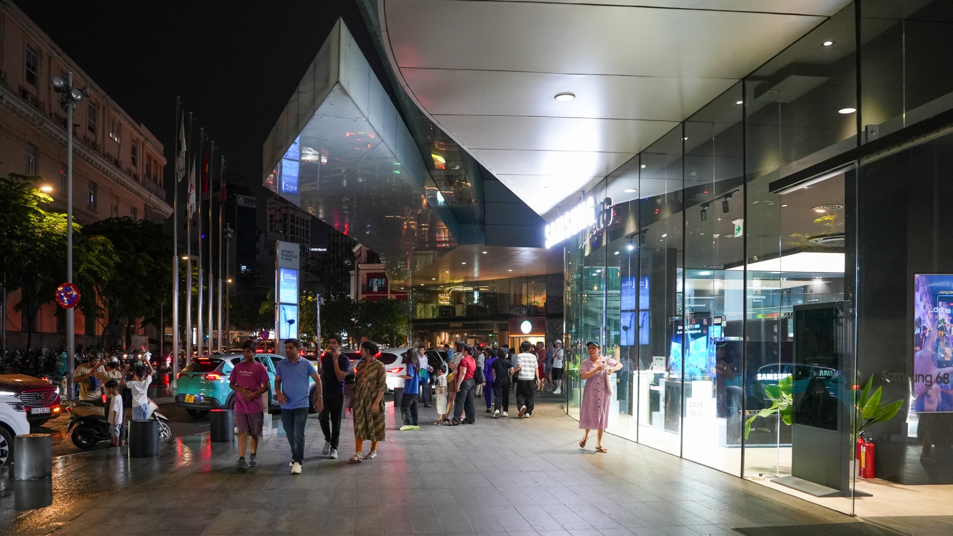 Evening crowd in front of a modern glass arcade near Bitexco Financial Tower on Nguyen Hue Walking Street, District 1, Ho Chi Minh City