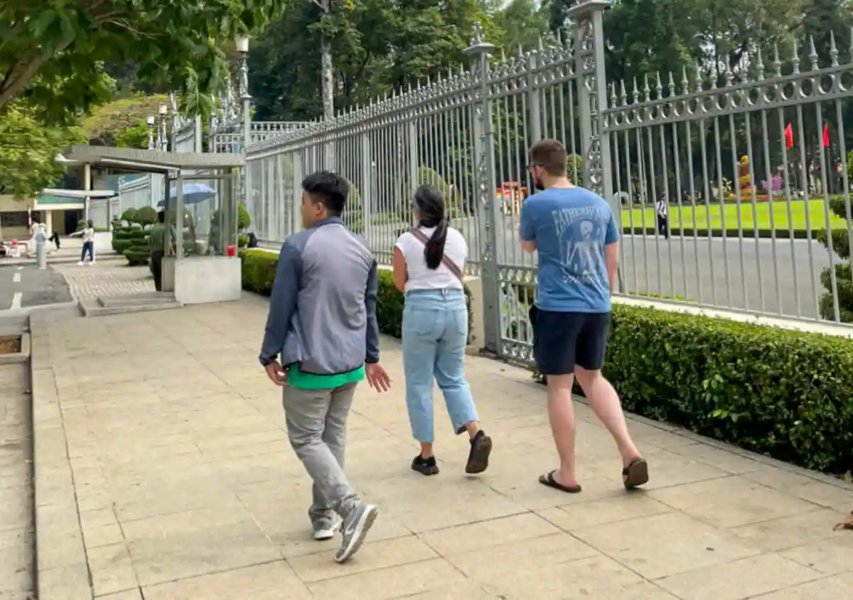 Travellers and a local guide walking together along the fence of Independence Palace on a Free Walking Tour in Ho Chi Minh City