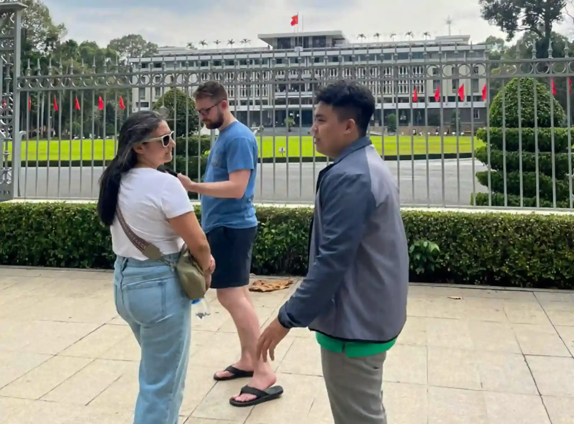 Local guide telling the story of Independence Palace to two travellers standing at the main gate in District 1, Ho Chi Minh City